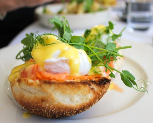 : Plato de huevos Benedict con salsa holandesa con estragón sobre mollete de cristal y ensalada de canónigos