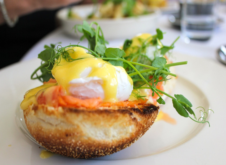 : Plato de huevos Benedict con salsa holandesa con estragón sobre mollete de cristal y ensalada de canónigos